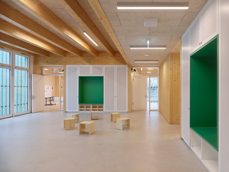Interior classroom with exposed timber beams, plywood partitions with green alcoves, and light wood benches