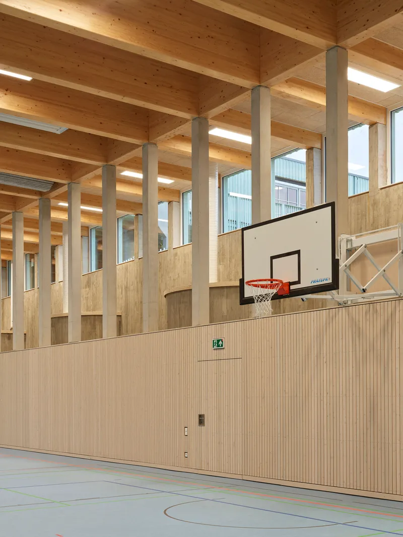 Gymnasium interior with basketball hoop, light wood paneled walls, and exposed timber post and beam ceiling