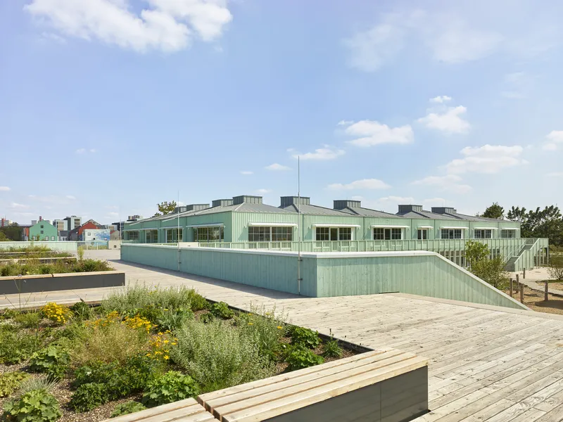 Rooftop garden with planted beds and pale green corrugated metal facade under a partly cloudy sky