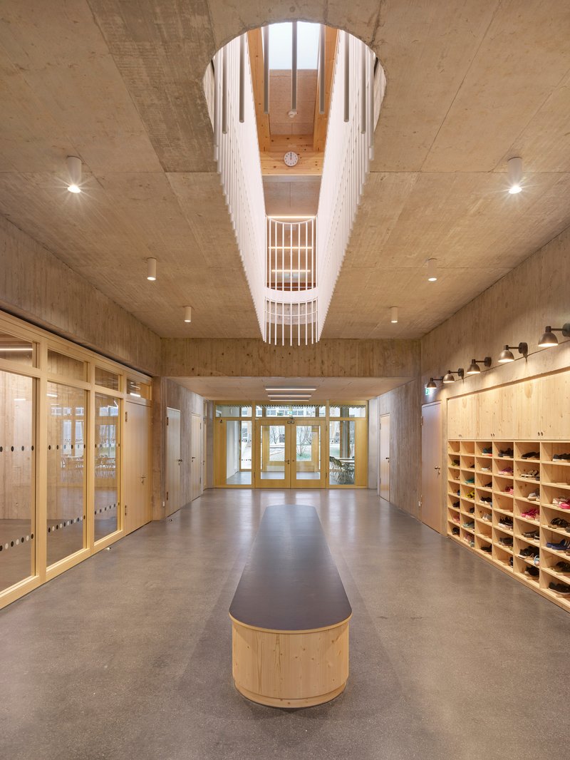 Entry corridor with cylindrical skylight above a curved bench under exposed concrete ceilings