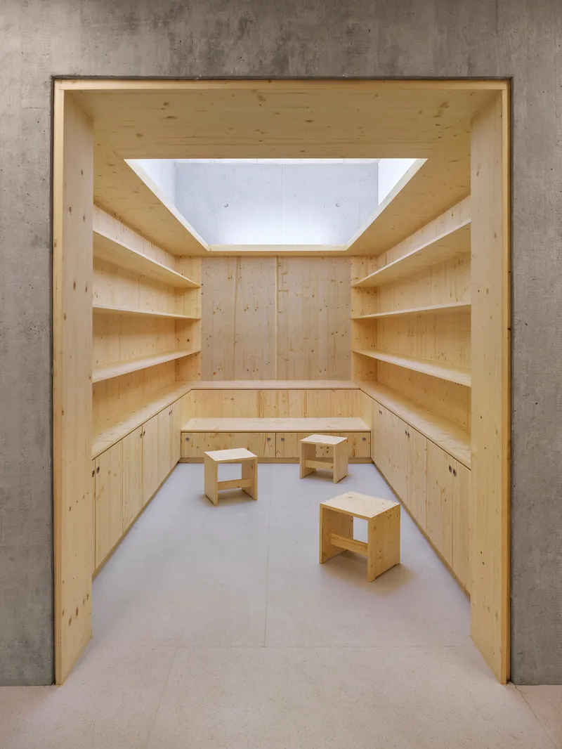 Pine shelving alcove framed by concrete walls with a central skylight above three stools