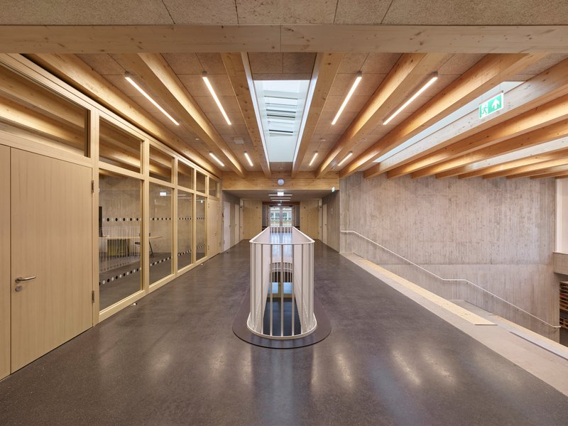 Corridor with exposed timber beams and cylindrical void beneath linear skylights and pendant lights
