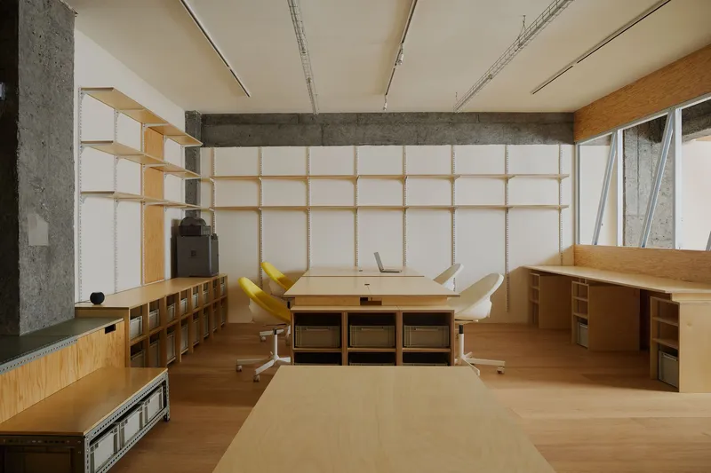 Workspace with plywood desk and shelving units beneath a timber and fabric grid wall system