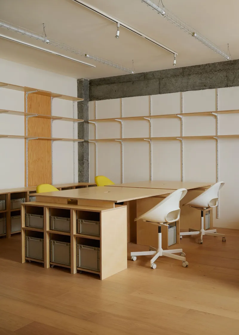 Plywood desk with integrated storage cubes and office chairs against a modular fabric panel wall