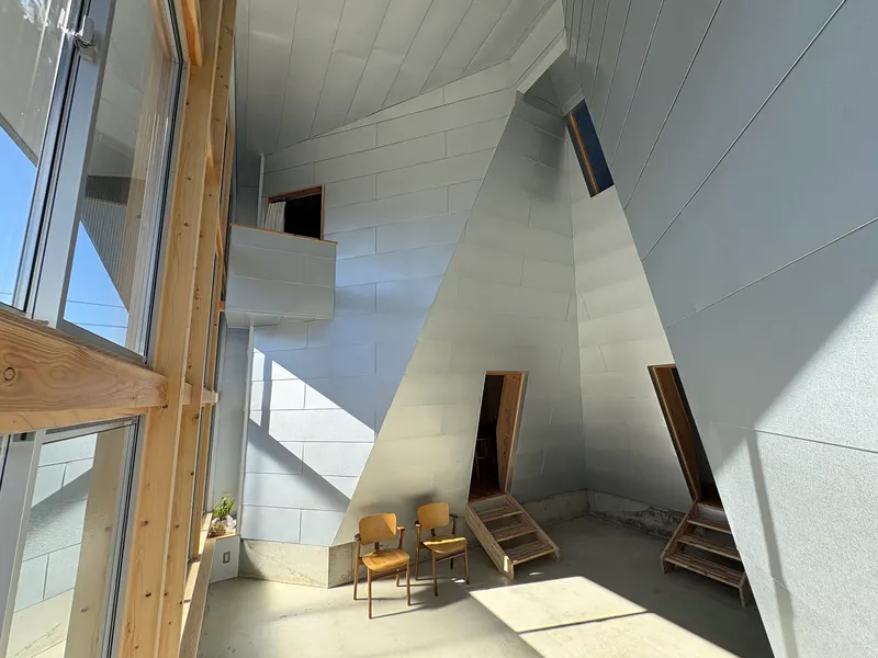 Double-height interior space with angled white panel walls and timber framed openings in bright daylight