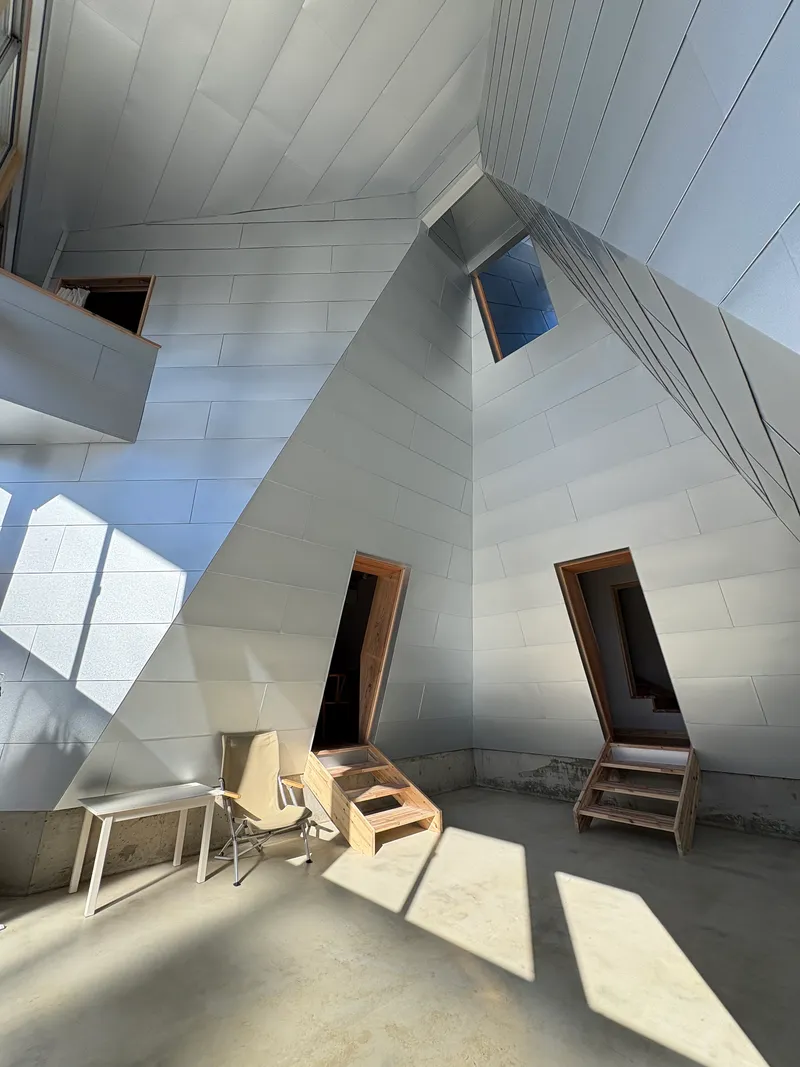 View of the faceted white panel ceiling and timber doorways casting sharp shadows on concrete floor