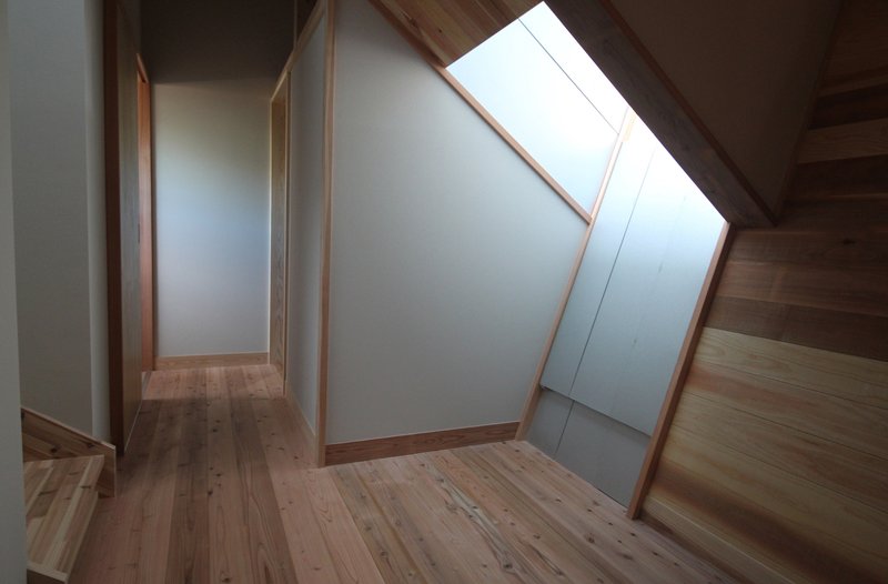 Upper hallway with angled skylight framed in timber and white painted walls meeting wood flooring