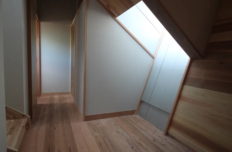 Upper hallway with angled skylight framed in timber and white painted walls meeting wood flooring