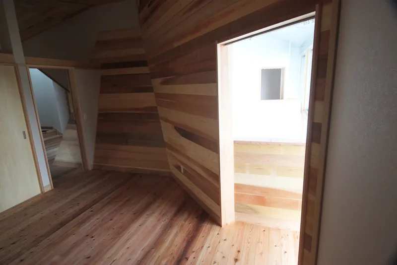 Corner room with horizontal timber plank walls and doorway opening to an adjacent sunlit space