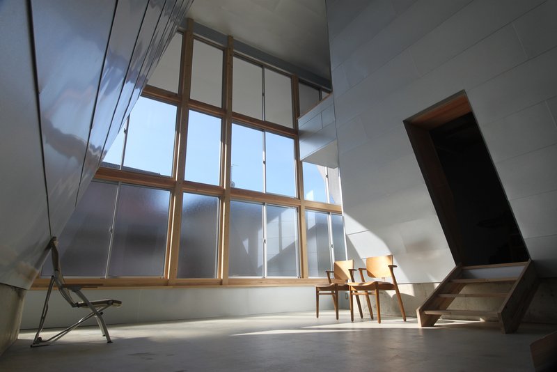 Double-height interior space with timber-framed window wall and angled ceiling planes under bright daylight
