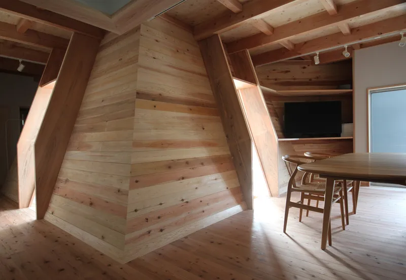 Angled timber-clad wall meeting exposed beam ceiling and dining area with track lighting overhead