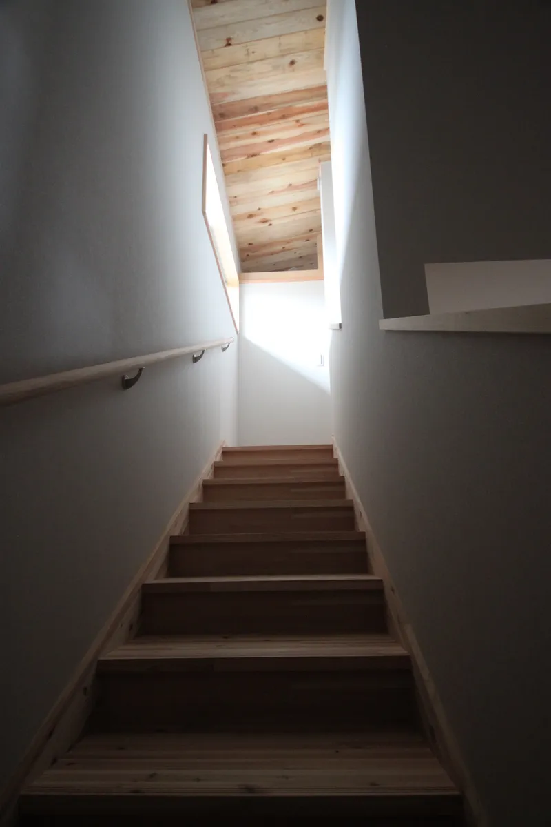 Timber staircase ascending between white walls toward an exposed wood ceiling and skylight above