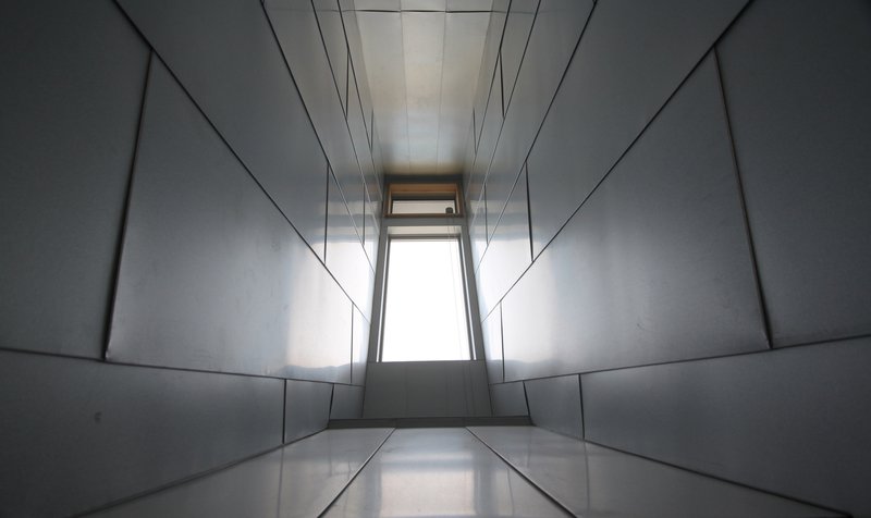 Narrow corridor lined with metal panels converging toward a distant window at the end