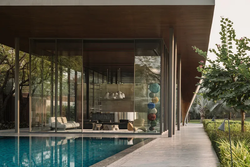 Poolside terrace with floor-to-ceiling glass walls reflecting the water and surrounding plantings