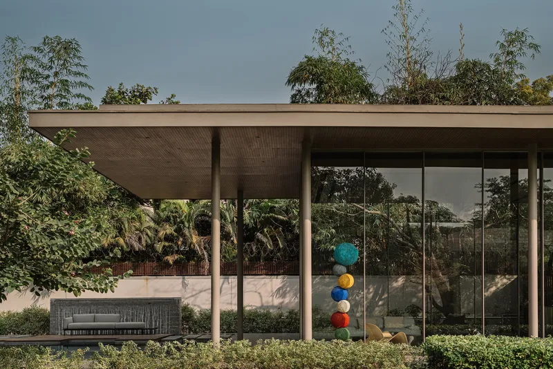 Covered terrace with timber-lined soffit and glass walls framing a sculpture beneath an overcast sky