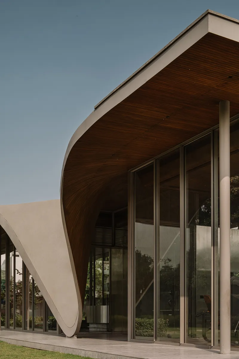Close-up of the sculptural roof overhang with timber soffit meeting glass curtain wall below