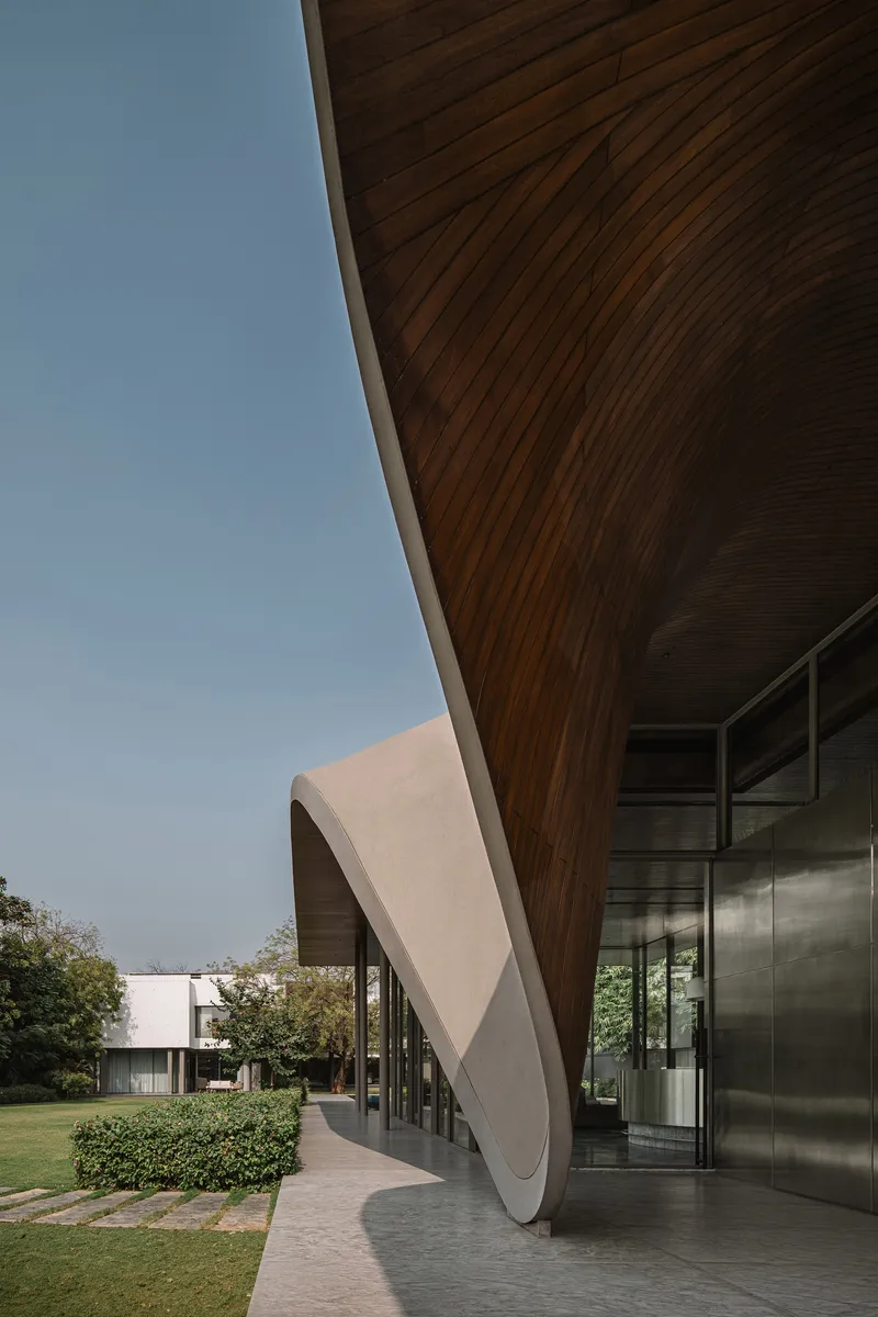 View along the underside of the curving timber roof canopy extending toward adjacent lawn and hedges