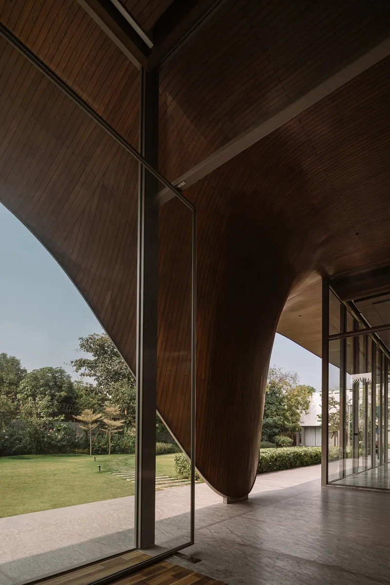 Interior view through open glass doors showing timber soffit curving down to meet polished concrete floor