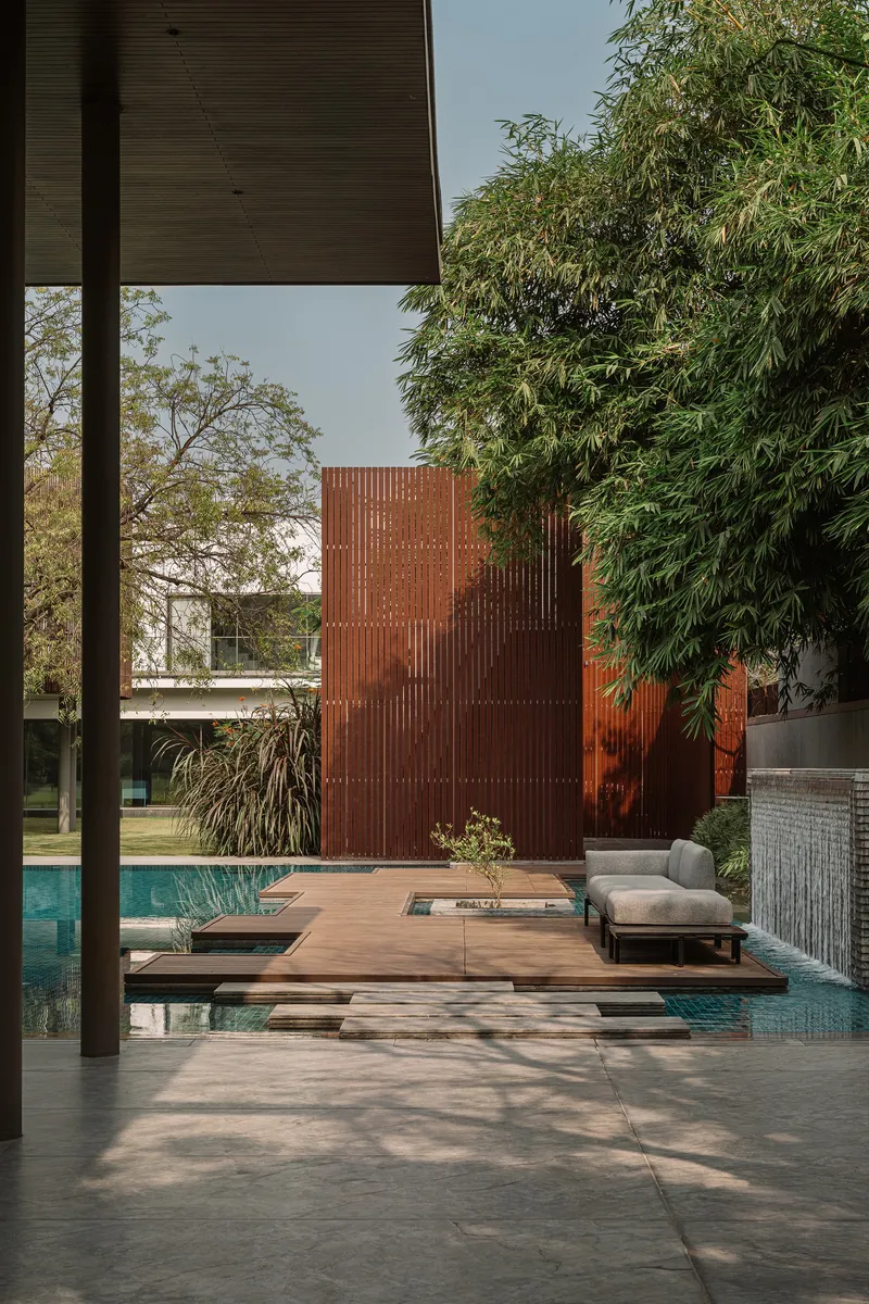 Timber deck platforms extending over the pool toward a perforated corten steel screen wall