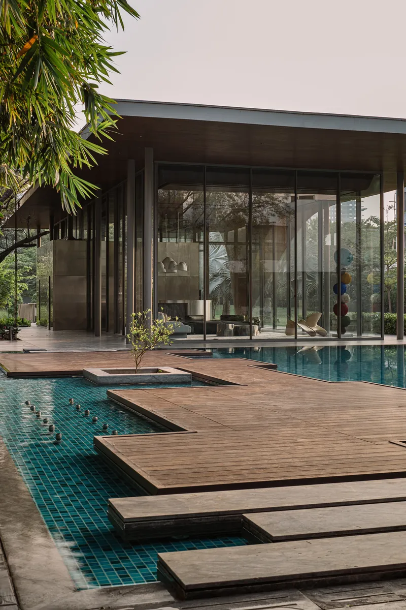 Stepped timber decking crossing the pool beneath a glass-walled pavilion with overhanging roof and bamboo above
