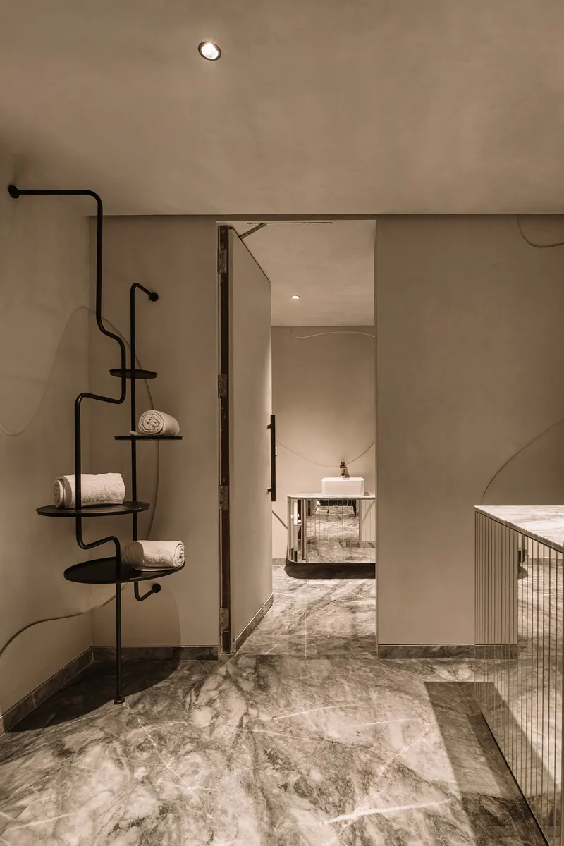 Interior threshold with black metal shelving unit beside grey marble floor and doorway to adjacent room
