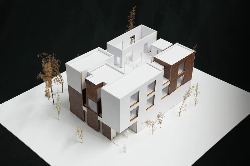 Physical model showing clustered volumes with white and brick facades surrounded by miniature trees