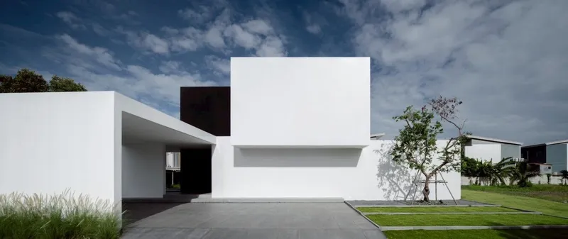 Street view of the white stucco volumes with cantilever and recessed entry under scattered clouds