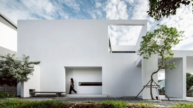 White stucco facade with rectangular voids and recessed entry as a figure walks through the courtyard