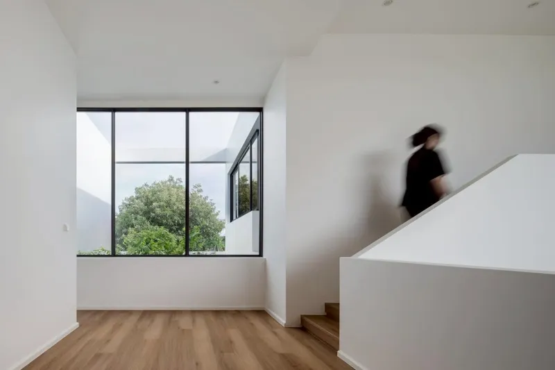 Stair landing with a figure descending and large black-framed window overlooking treetops