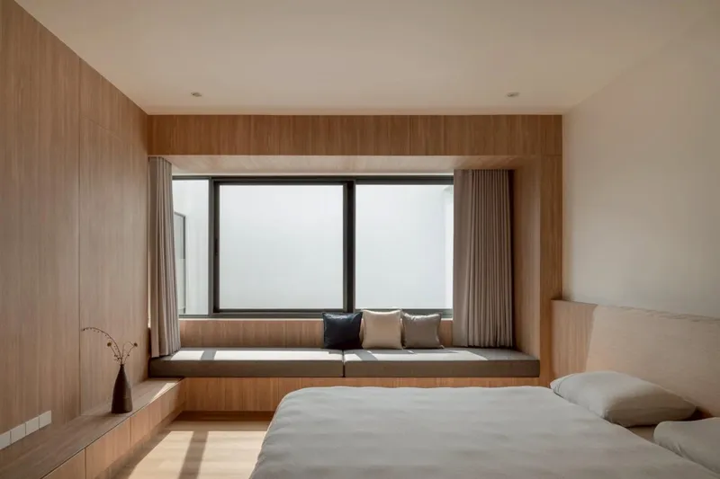Bedroom with timber-framed window seat overlooking an overcast sky and low platform bed
