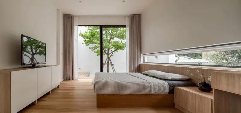 Bedroom looking toward a glazed door opening onto a timber deck with courtyard trees