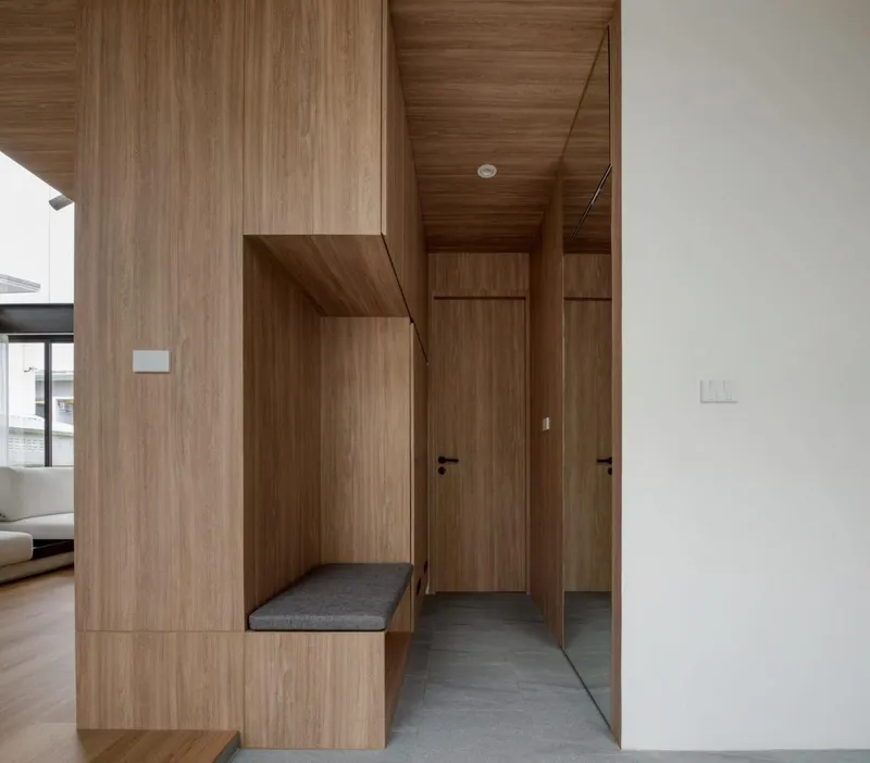 Entry hallway clad entirely in timber veneer with built-in bench and grey stone flooring