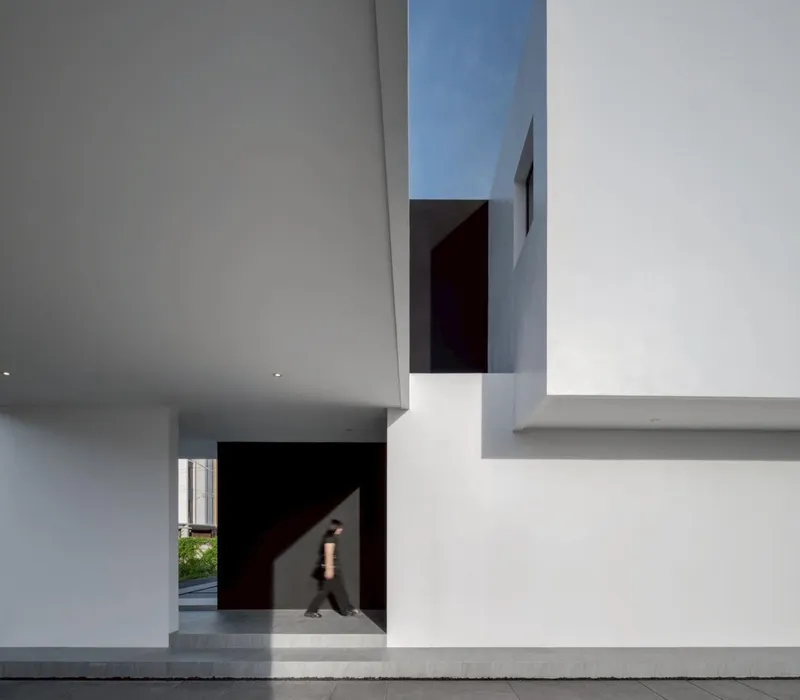 Double-height interior space with skylight slot and figure walking through doorway in shadow