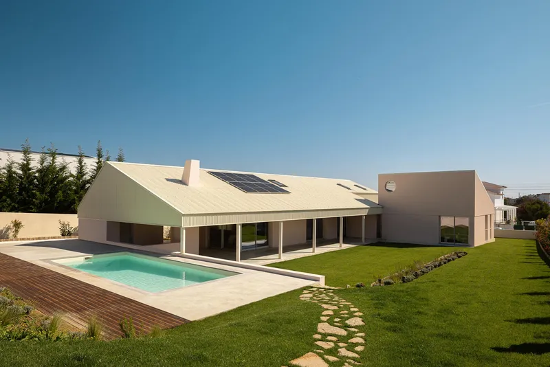 Rear facade with corrugated metal gable roof, solar panels, pool, and stepping stone path through lawn