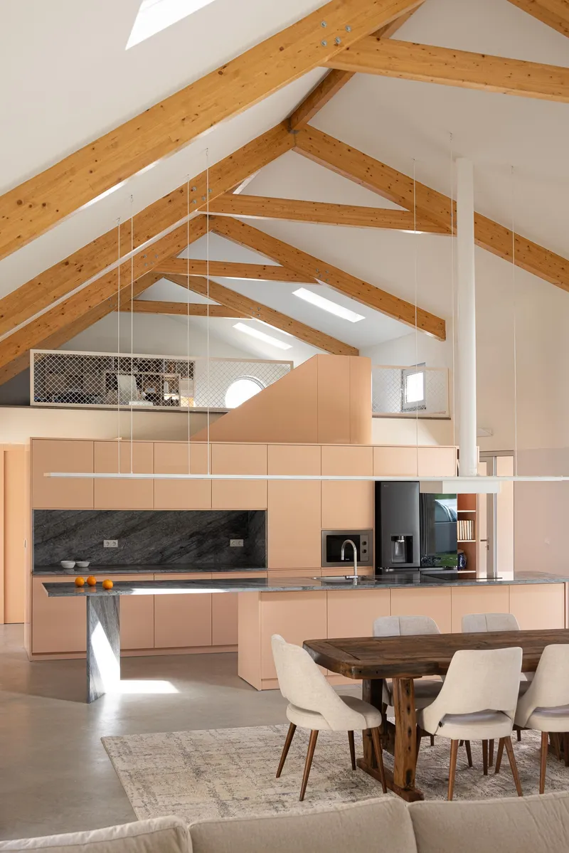 Open kitchen and dining area under vaulted timber ceiling with skylights and mezzanine storage above