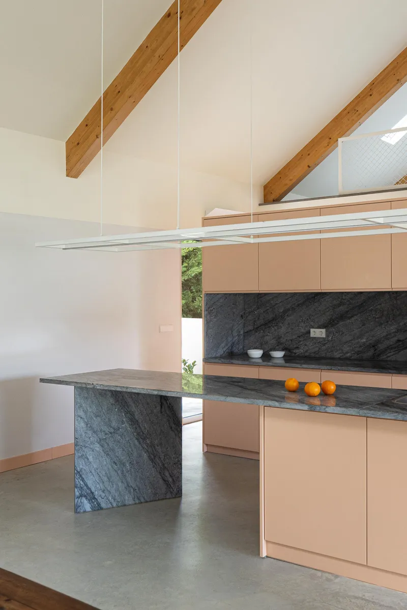 Kitchen with pale pink cabinets, black marble island and backsplash, exposed timber beams overhead