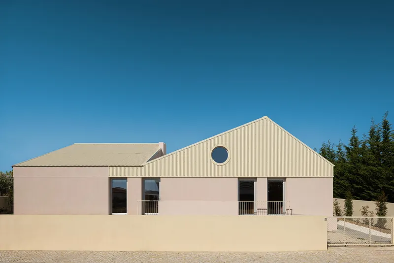Street elevation showing pink stucco walls with a circular window and corrugated metal gable roof