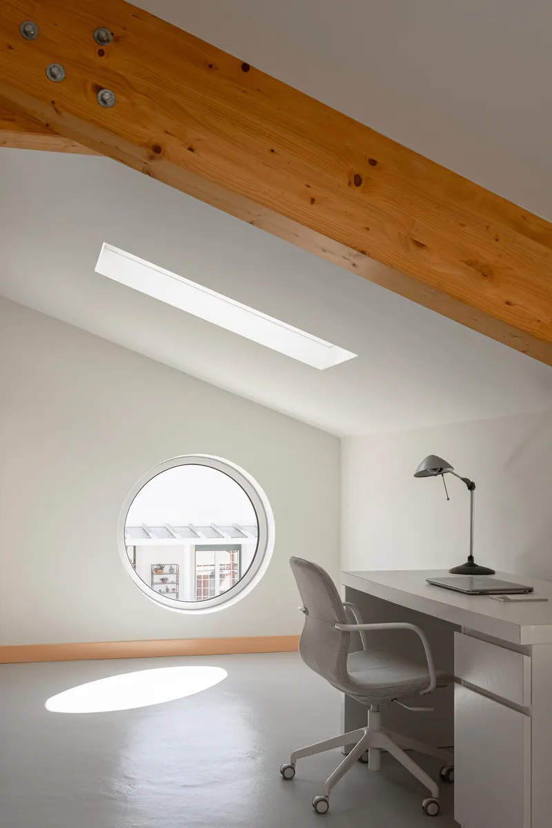Study corner with circular window and exposed timber beam beneath a skylight slot