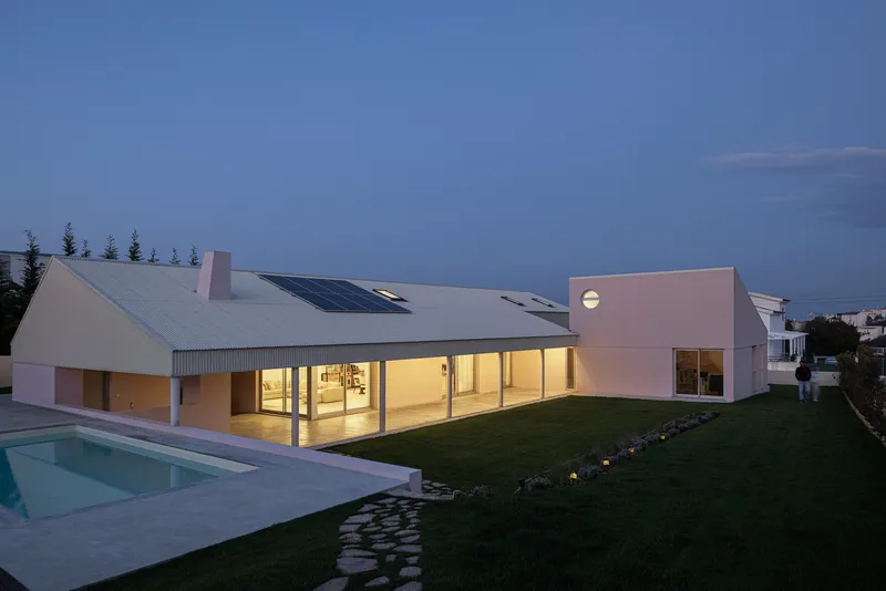 Rear view of the white gabled residence with full-height glazing and swimming pool at twilight