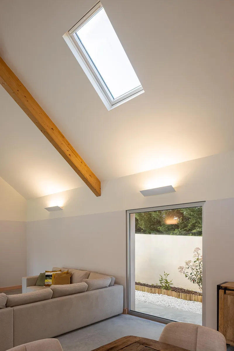 Living room with vaulted ceiling, exposed timber beam, skylight and glazed door to courtyard
