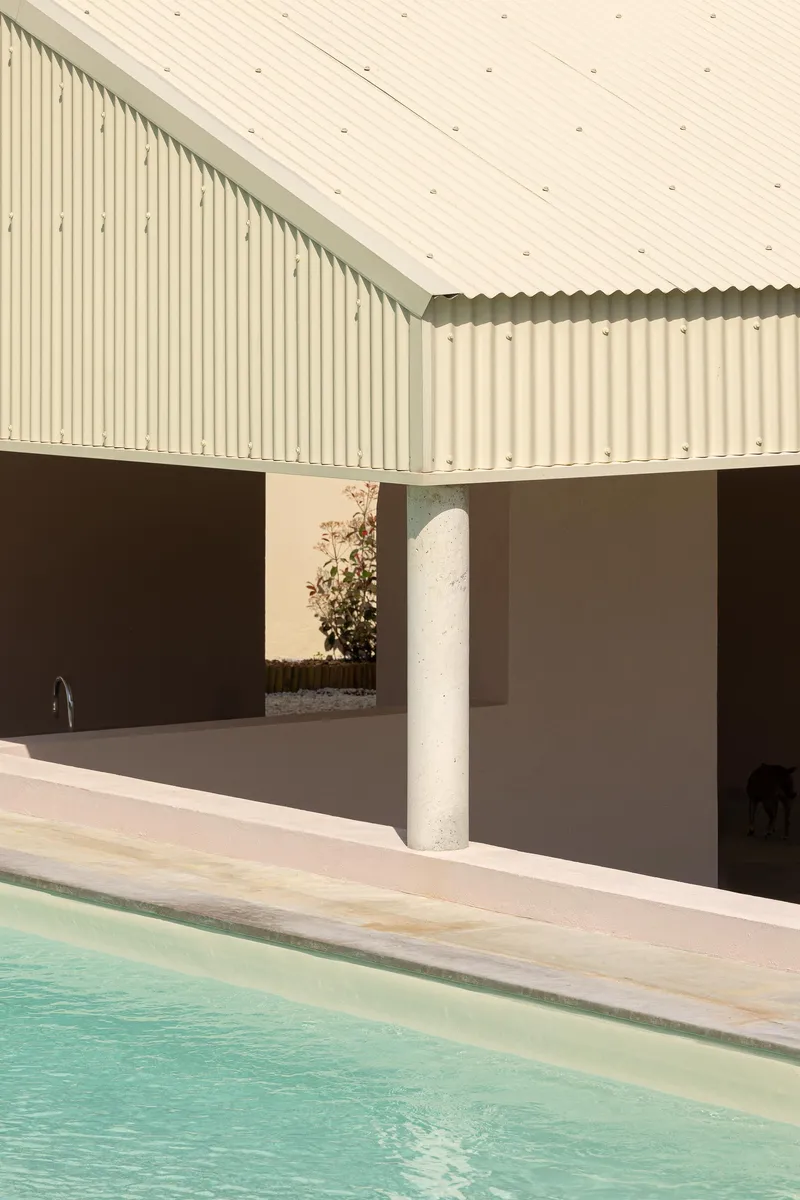 Pool edge with white corrugated metal soffit supported by a cylindrical column in afternoon light