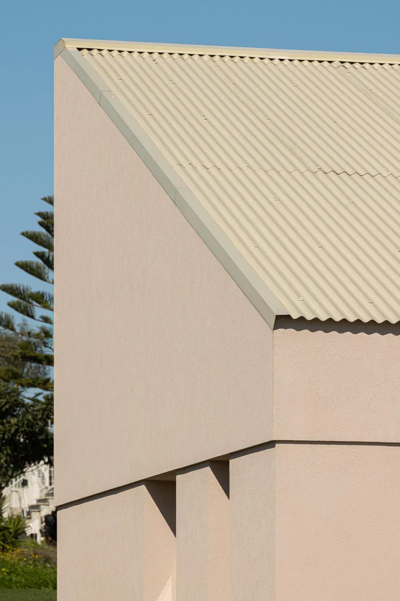 Corner detail of corrugated metal roof overhang meeting a pink stucco wall under clear blue sky