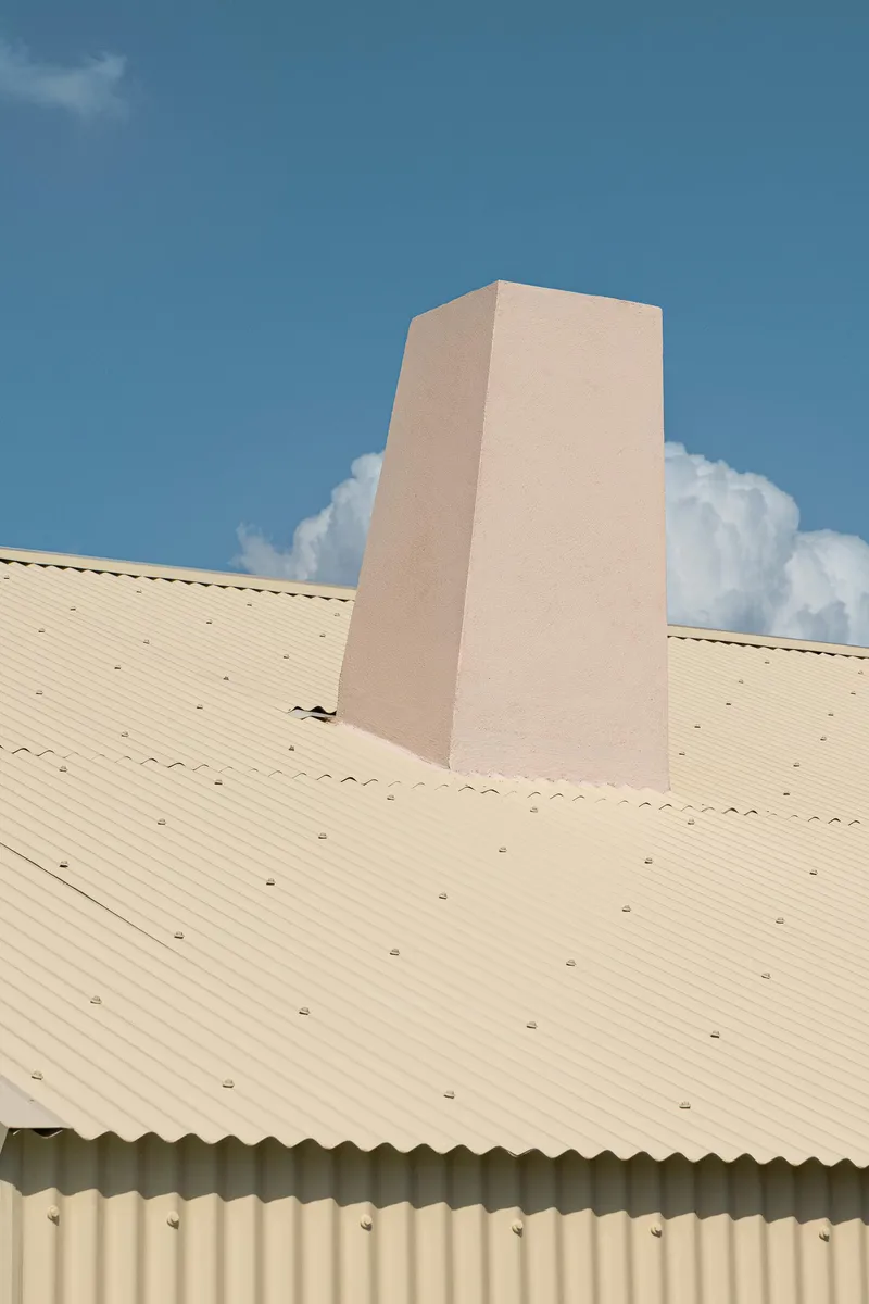 Tapered pink stucco chimney rising from a corrugated metal roof against white clouds