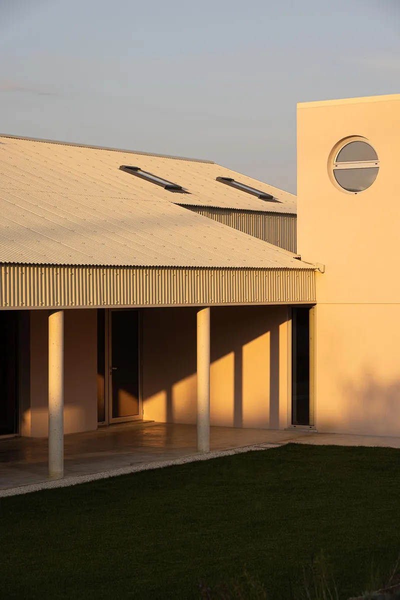 Covered terrace with column shadows stretching across floor at sunset beside circular window