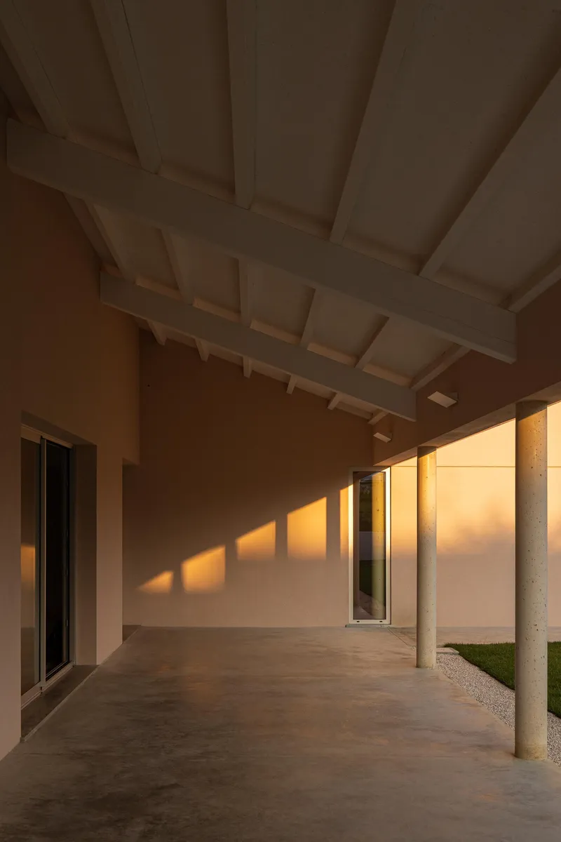 Covered walkway with exposed timber rafters and concrete columns casting long shadows in afternoon light