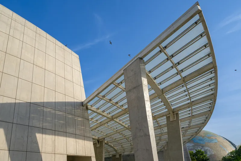 Curved canopy with exposed steel ribs and concrete columns against a clear blue sky