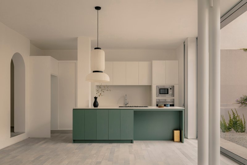 Kitchen with green island cabinetry and white upper cabinets beneath pendant light