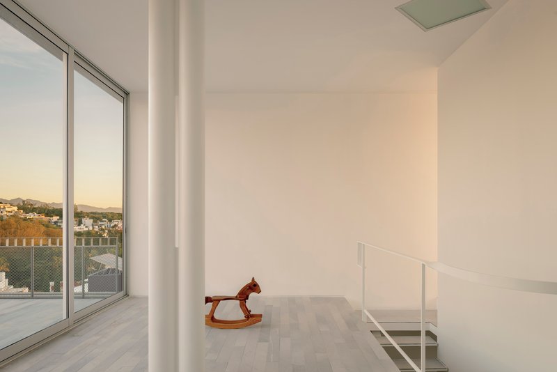 Upper floor landing with glass balustrade and rocking horse beside glazed opening at sunset