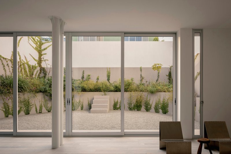 View from interior living space through glazed doors to courtyard with planted beds and steps
