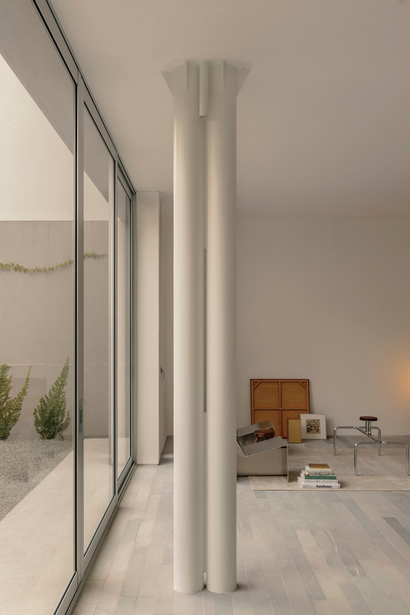 Interior view of a cylindrical white column with integrated lighting beside floor-to-ceiling glazing overlooking a courtyard